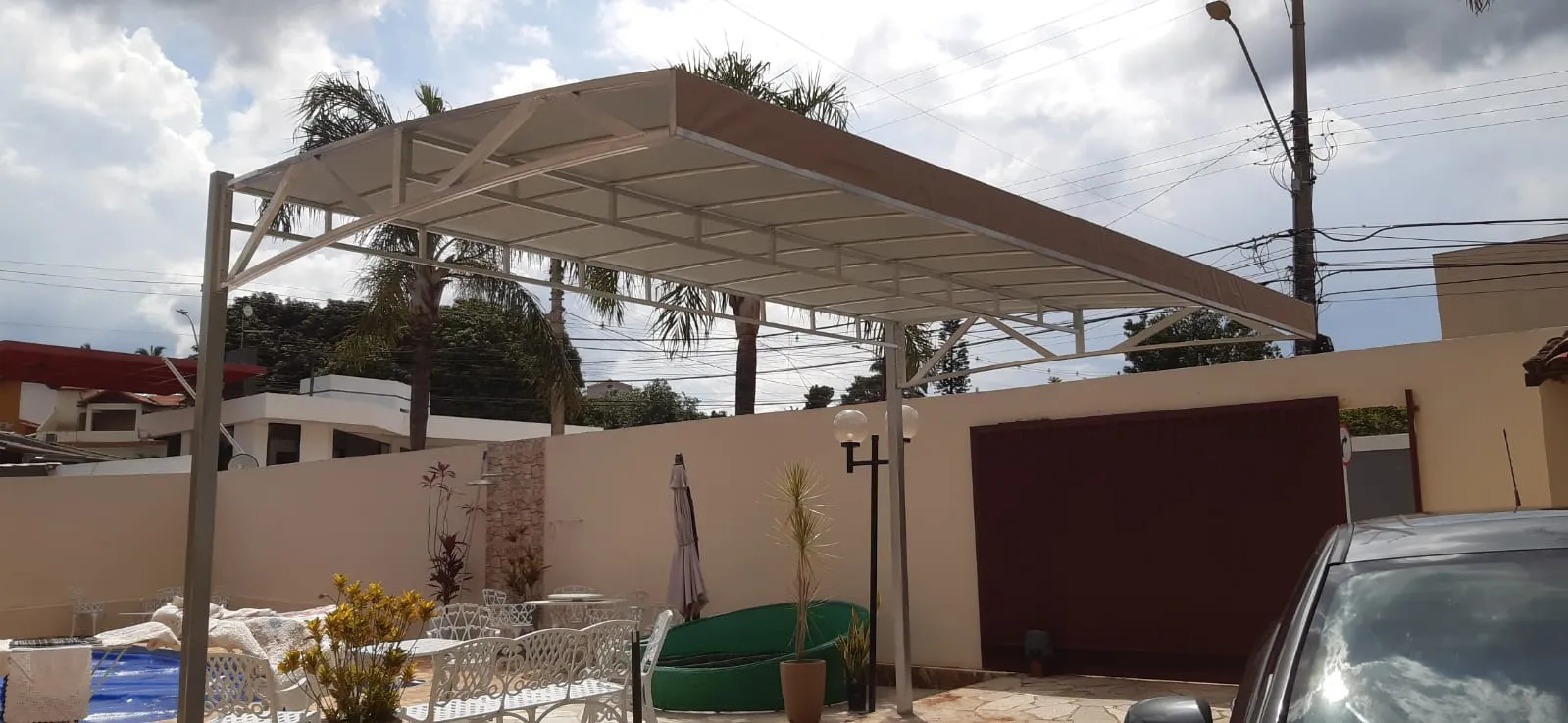 Cobertura fixa em lona tom areia sobre área de lazer com móveis de jardim