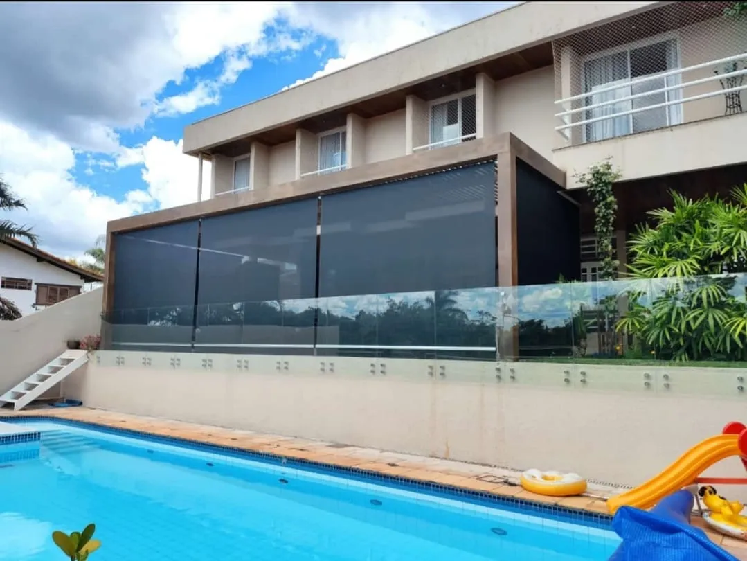 Toldo cortina cinza-escuro em varanda envidraçada sobre piscina