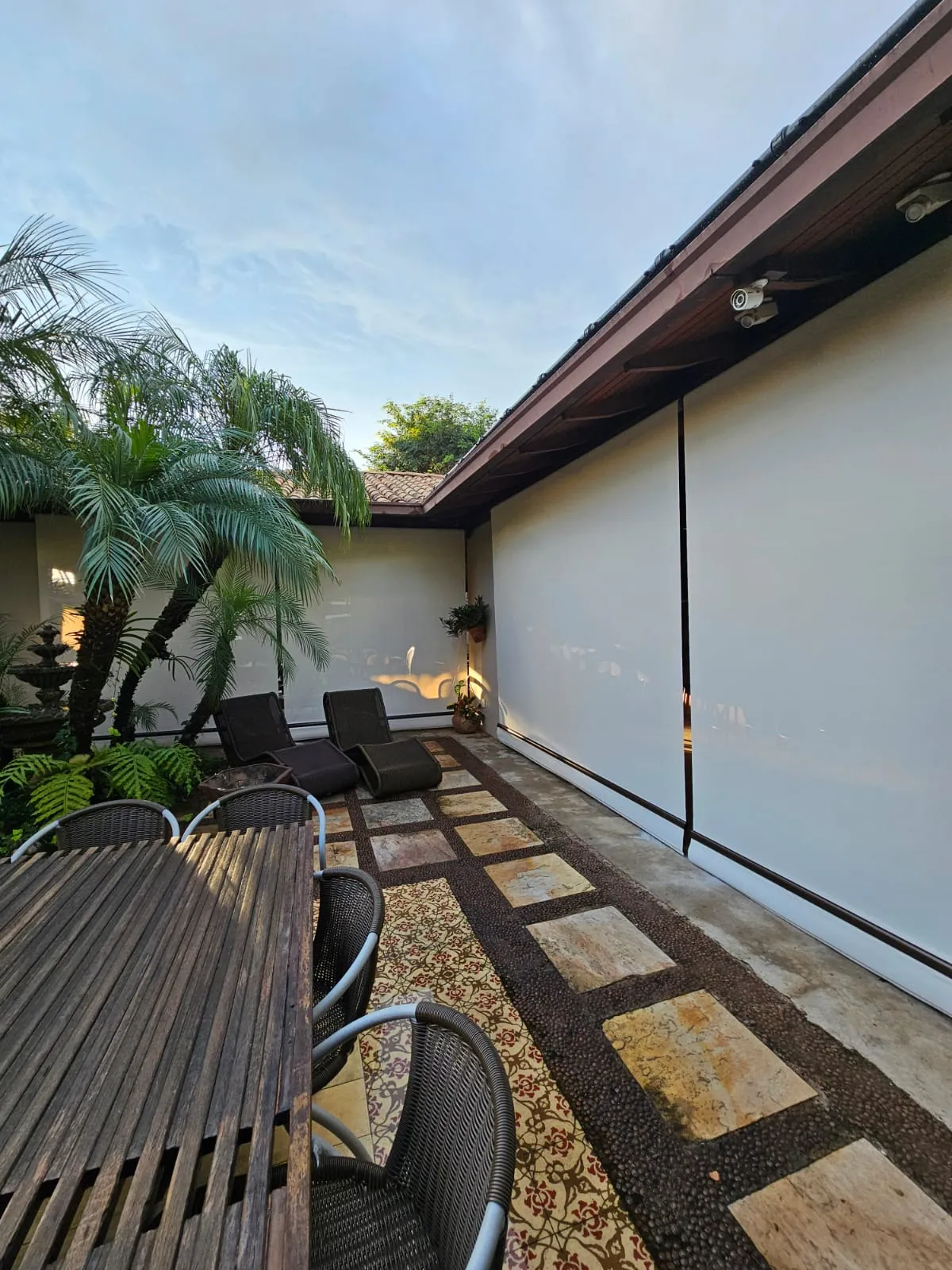 Toldo cortina branco em pátio com fonte e palmeiras