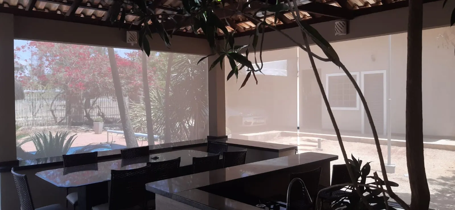 Toldo cortina com tela solar recolhida em área gourmet com vista de piscina