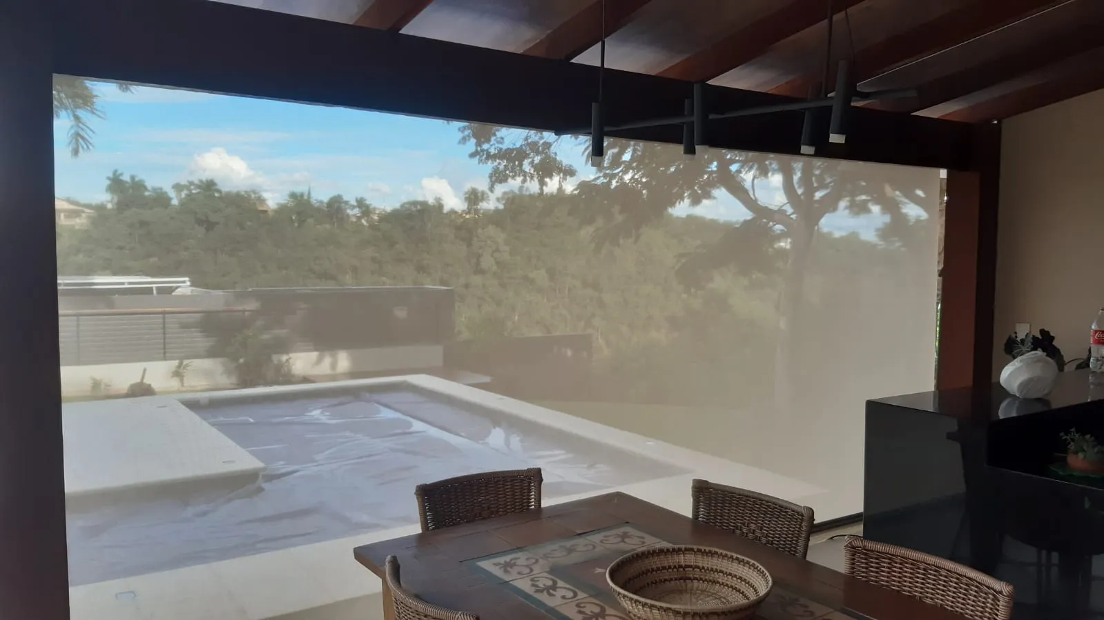 Toldo cortina com tela solar fechada em área gourmet com vista de piscina