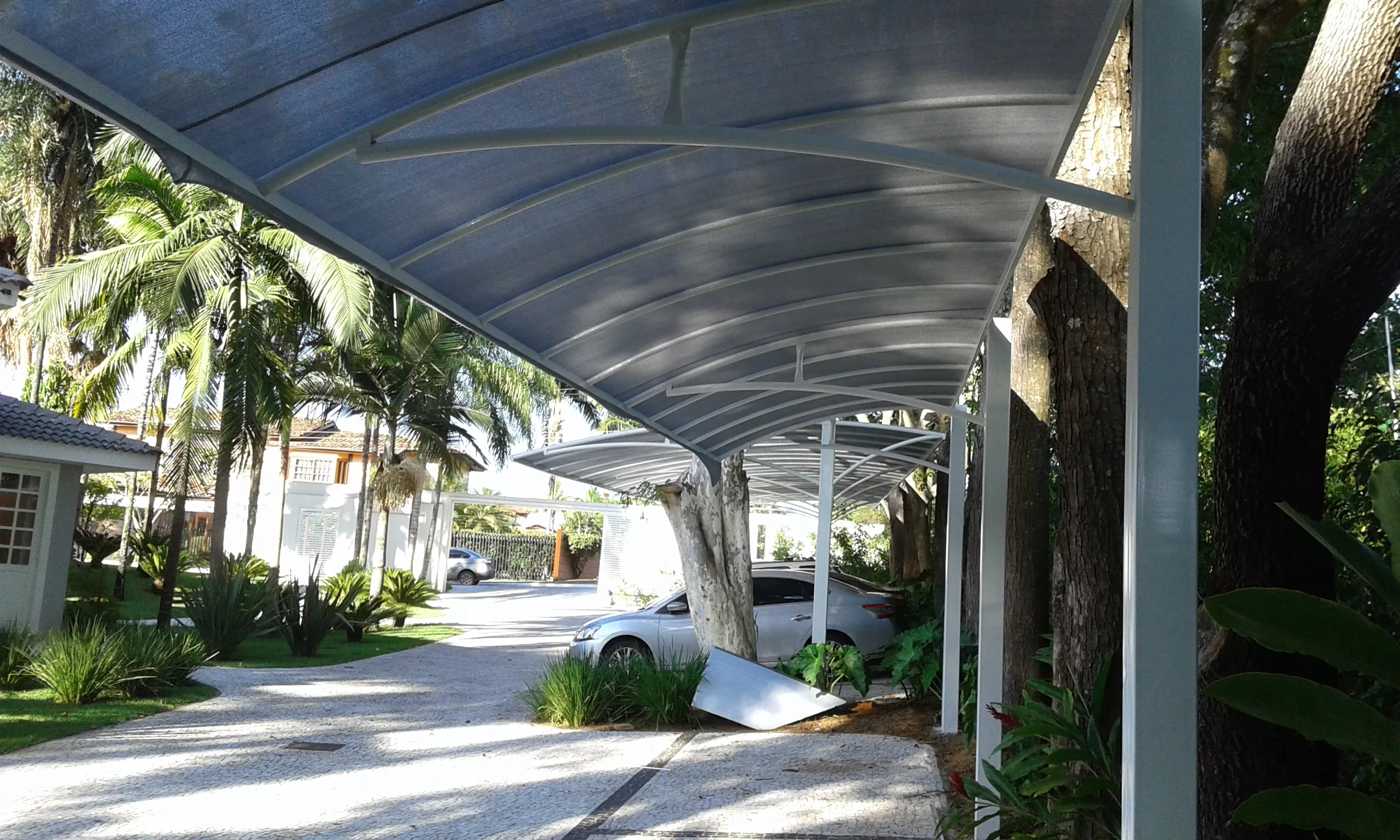 Sombrite em carport residencial entre palmeiras